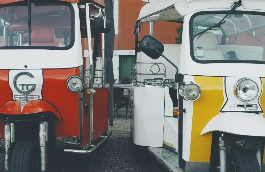 durante o dia, um tuk-tuk vermelho e branco ao lado de um tuk-tuk amarelo e branco estacionados em rua de zurique