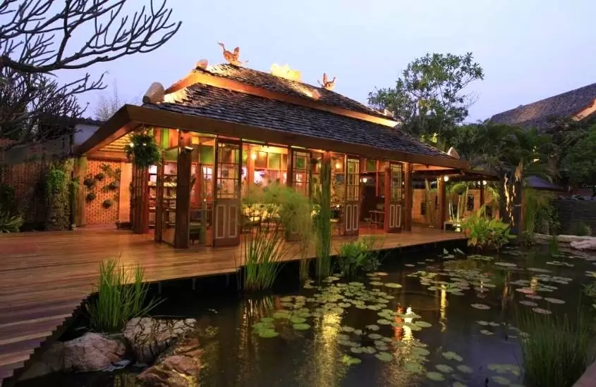 durante o entardecer, plantas em lago em frente a construção de madeira de um dos melhores hotéis em chiang mai perto do aeroporto