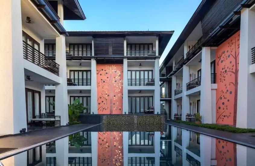 durante o dia, grande piscina cercada por construções brancas, com janelas e portas marrons em um dos hotéis em chiang mai