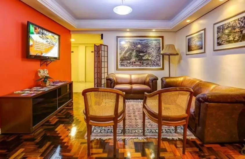 sofás e cadeiras marrons, em frente a tv pendurada em parede em sala de estar em um hotel barato em Porto Alegre