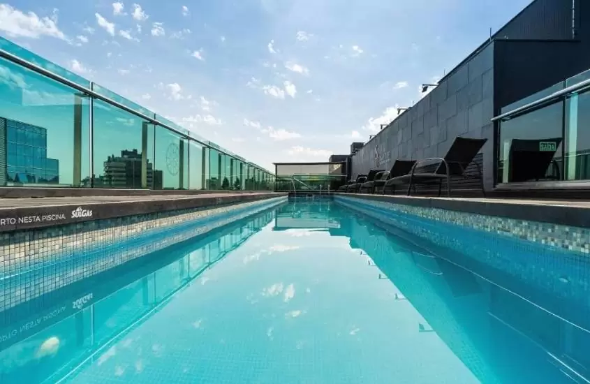 durante o dia, espreguiçadeiras pretas em frente a grande piscina em cobertura de um dos hotéis em porto alegre
