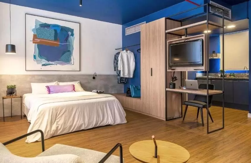 cama de casal, guarda-roupa e cozinha compactada em suíte de hotel