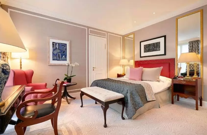 mesa e cadeira de madeira, poltrona vermelha em frente a cama de casal em suíte de um dos hotéis em zurique