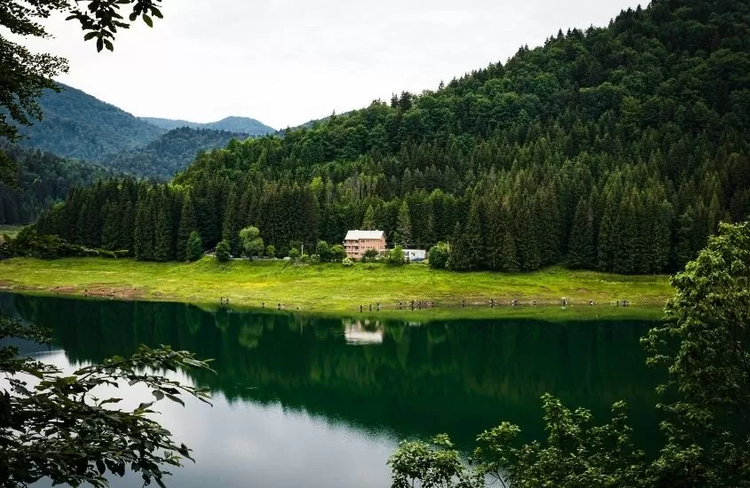 durante o dia, casa a beira lago em frente a montanha em uma das cidades na romênia