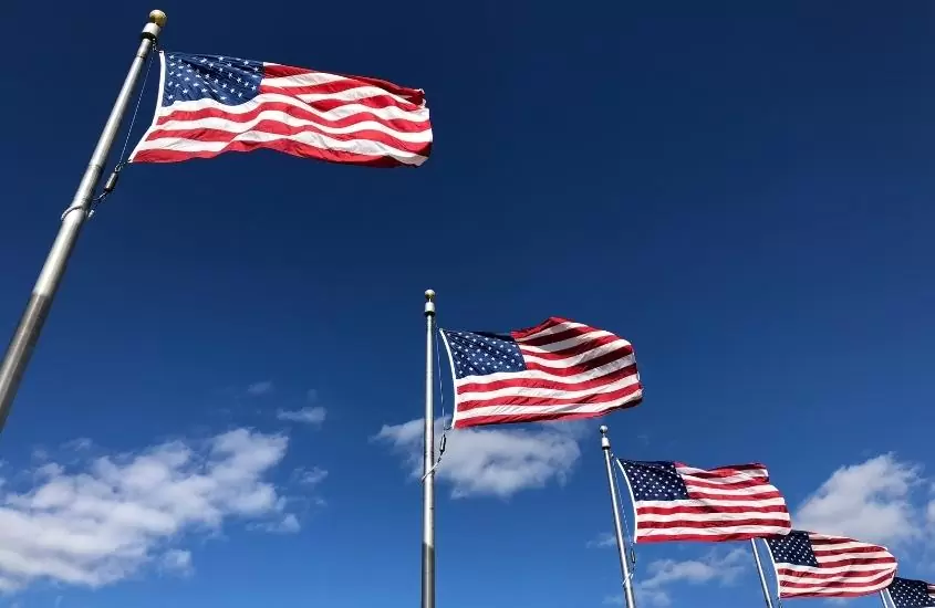 cinco bandeiras dos estados unidos hasteadas lado a lado, sob céu azul, durante o dia