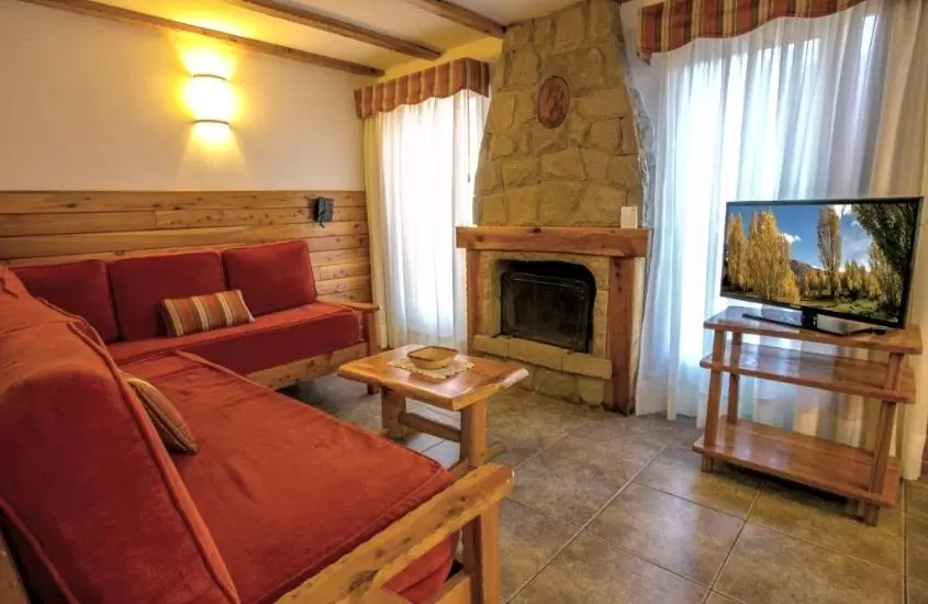 sofá vermelho em frente a lareira e televisão em hotel para turismo em bariloche