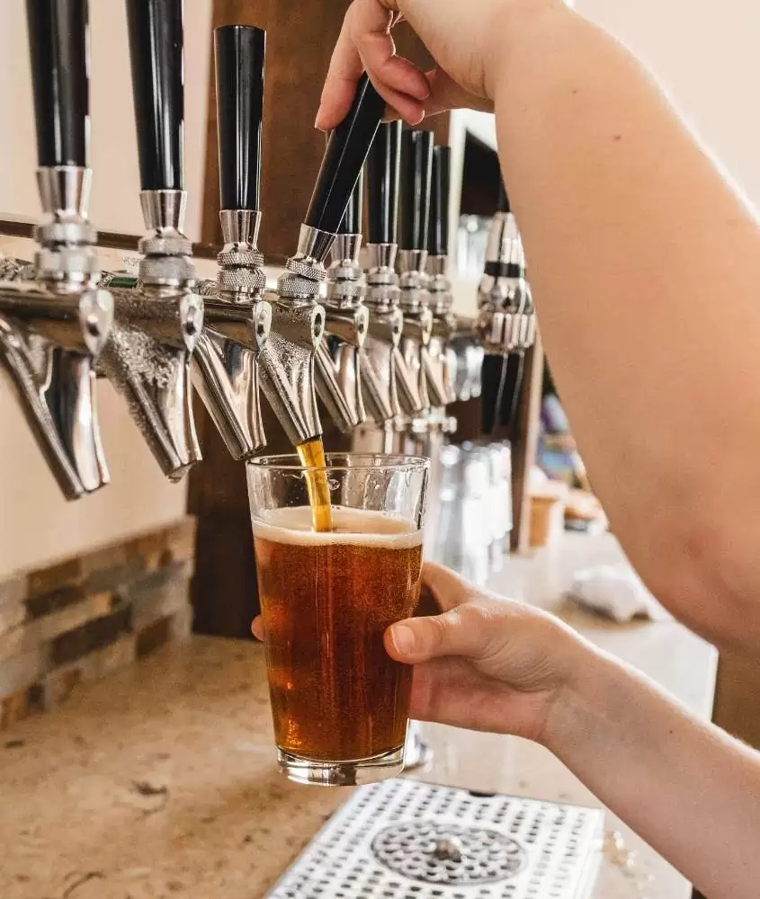 pessoa enchendo copo de vidro com cerveja artesanal em bar, lugar para quem busca o que fazer a noite em bariloch