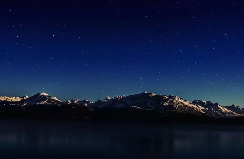 durante a noite, lago e montanhas cobertas de neve sob céu estrelado