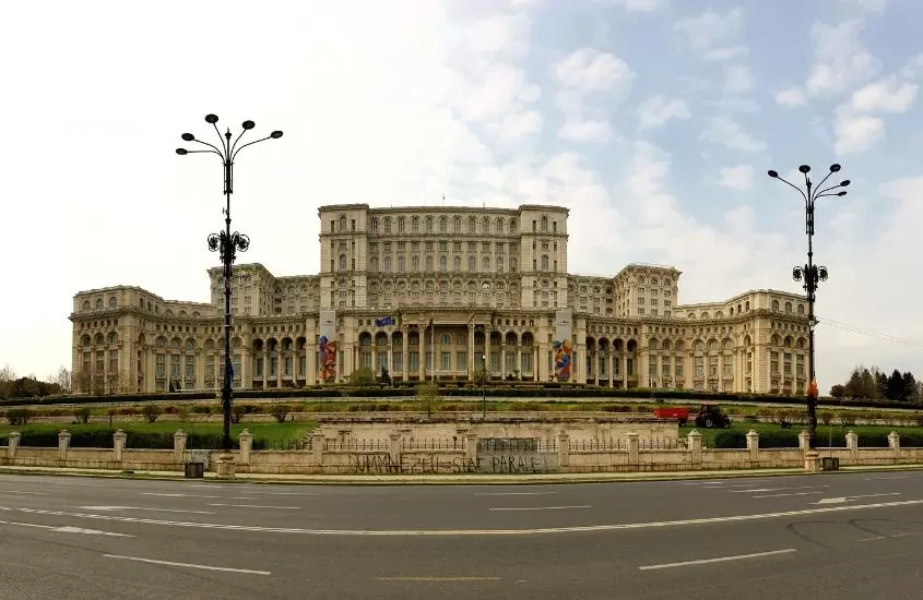 durante o dia, estrada vazia em frente a grande construção de concreto bege, de palácio do parlamento, um dos pontos turísticos da romênia