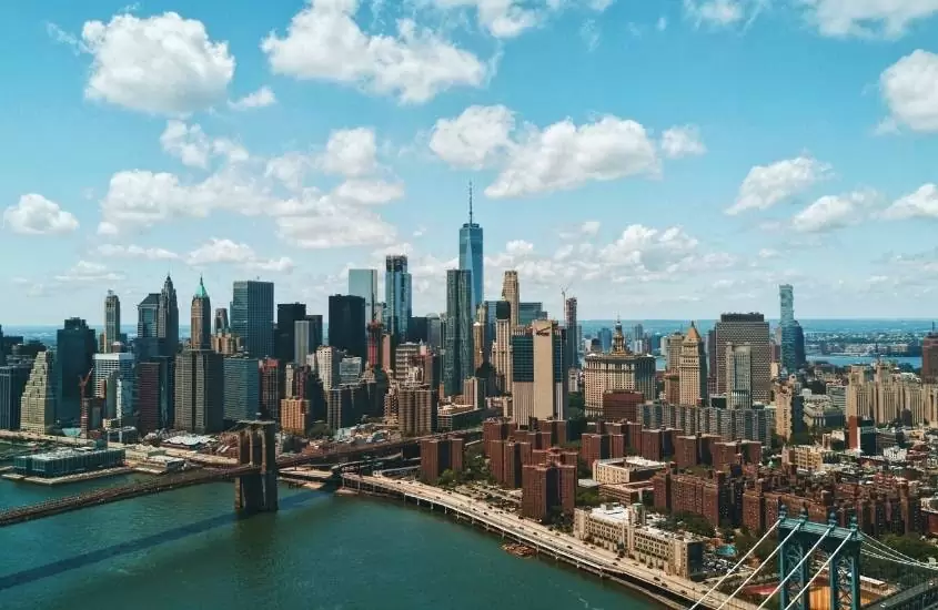 durante o dia, vista aérea de ponte sobre o mar, e ao fundo, diversos prédios em nova york