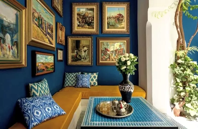 almofadas estampadas de azul em cima de sofá amarelo, encostado em parede azul cheia de quadros de arte