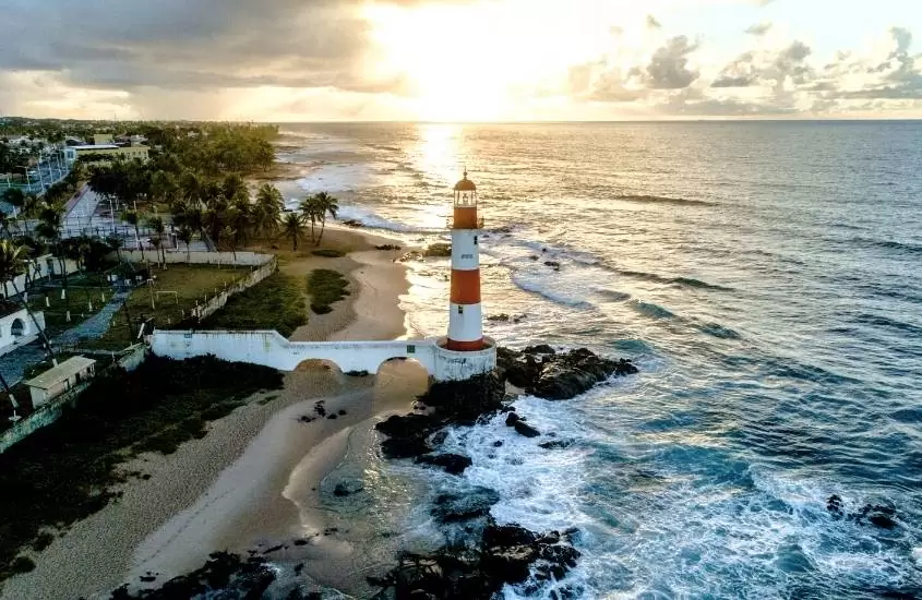 durante o dia, vista aérea de farol branco e laranja à beira-mar em praia de salvador, onde acontece o melhor réveillon do brasil