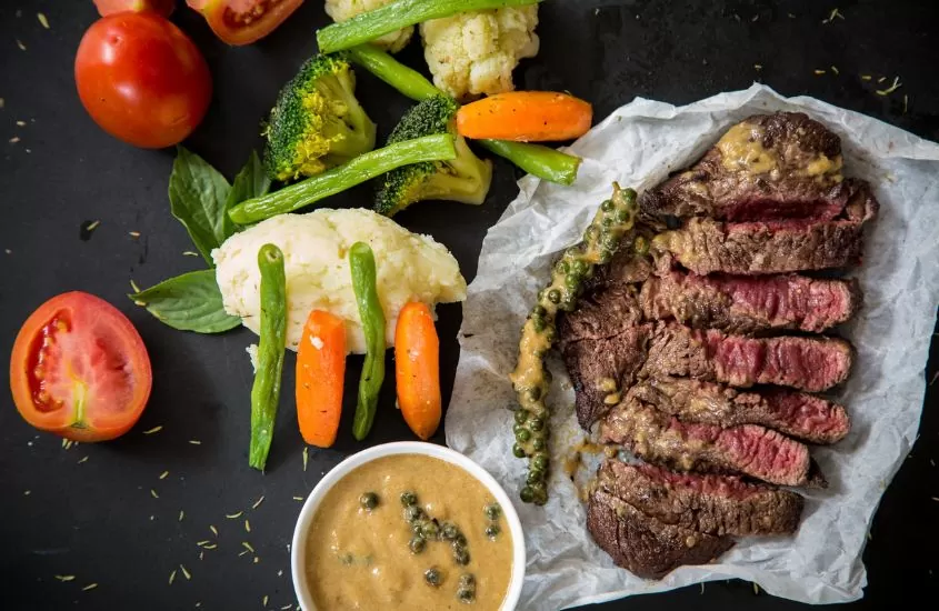 em cima de mesa preta, steak e legumes, um dos pratos típicos dos estados unidos