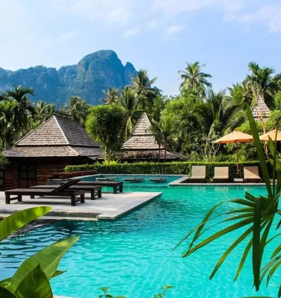 durante o dia, espreguiçadeiras ao redor de piscina, cercada por diversas árvores em um dos 25 resorts na Tailândia