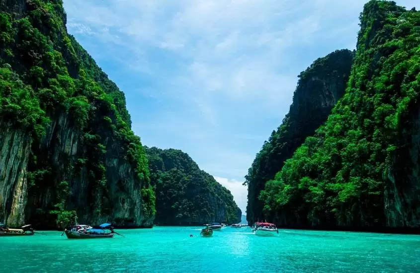 durante o dia, lanchas passando em mar azul turquesa, entre rochas de phuket, uma das melhores ilhas da tailândia