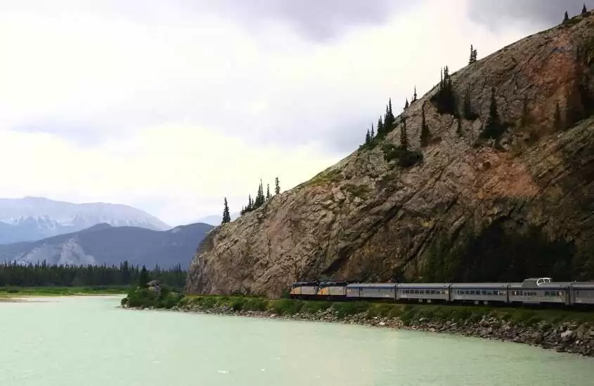 durante o dia, trem passando em trilho cercado por lago, do lado direito, e montanha, do lado esquerdo
