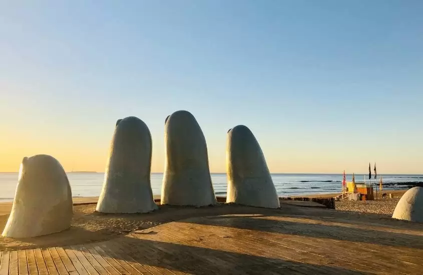 durante o dia, escultura de dedos saindo da areia, em frente ao mar
