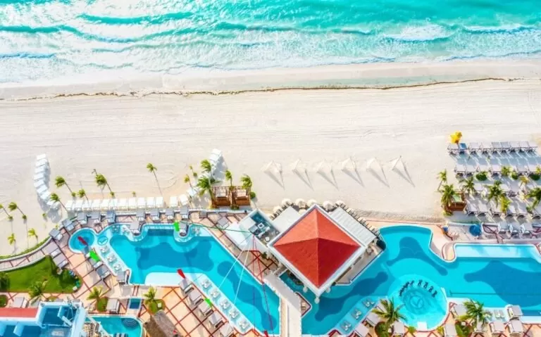 durante o dia, vista aérea de piscinas em área de lazer de um dos hotéis em cancun 5 estrelas com vista para o mar