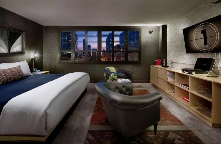 durante a noite, cama de casal e poltronas em frente a televisão, em suíte de um dos hotéis em toronto com vista para a cidade