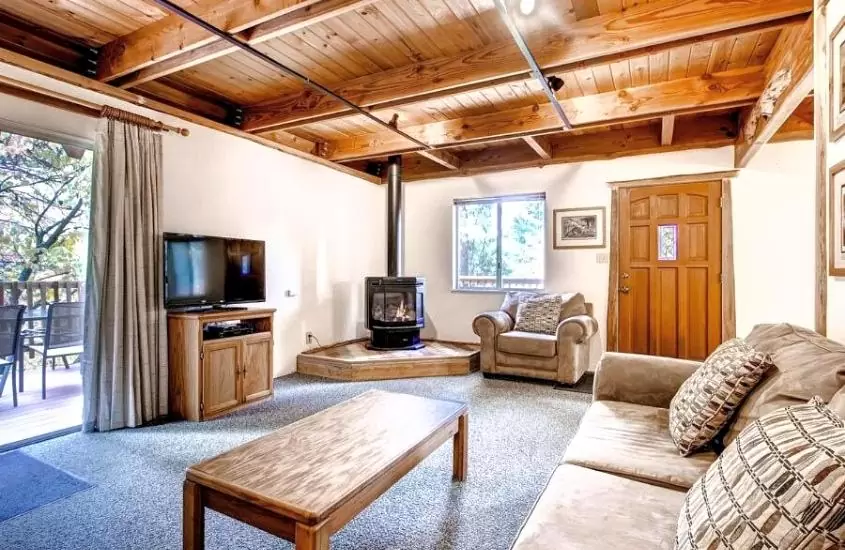 sofá, mesa de madeira, tv e lareira em sala de estar de uma das casas de temporada dentro do parque yosemite