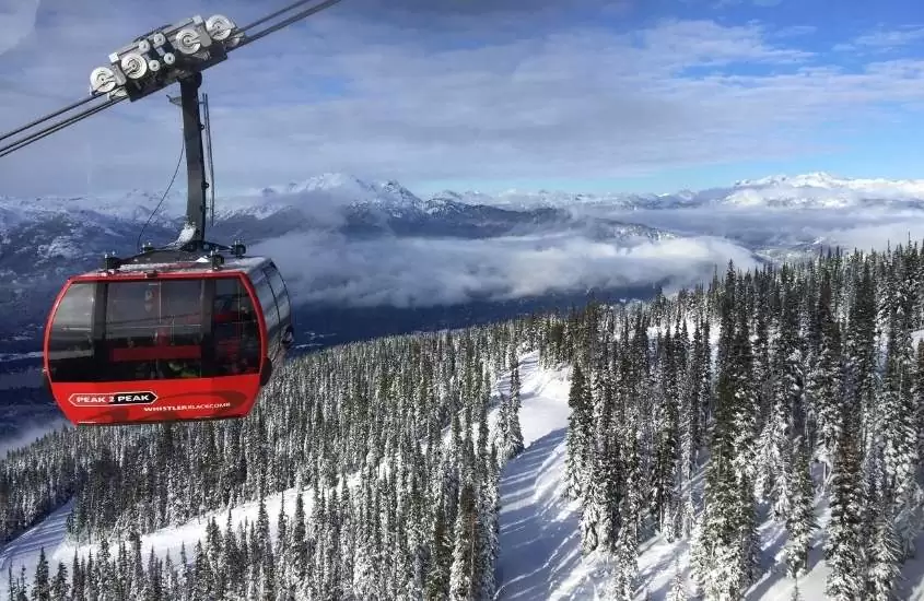 durante o dia, teleférico vermelho passando sobre montanha nevada em whistler, atrativo para quem busca o que fazer no Canadá