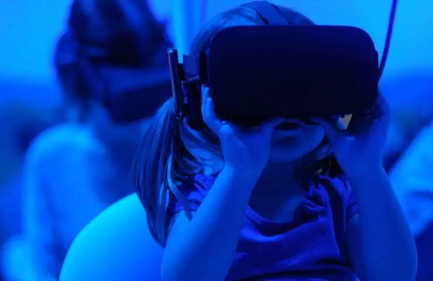 criança utilizando óculos de realidade virtual em museu iluminado por luz azul