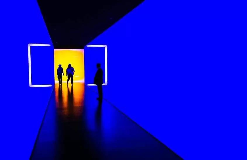 silhueta de pessoas caminhando em corredor de museu, iluminado por luz azul