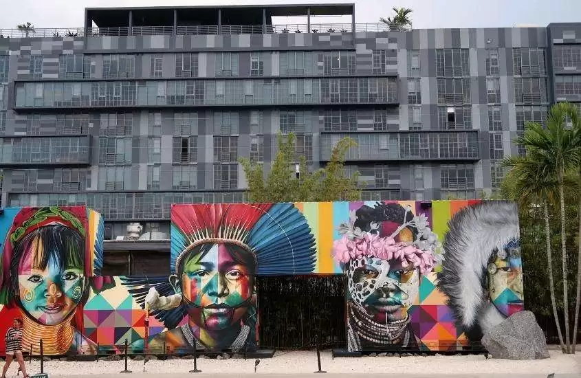 durante o dia, pessoa caminhando em frente a mural com grafites coloridos em Wynwood, atração para quem busca o que fazer em miami