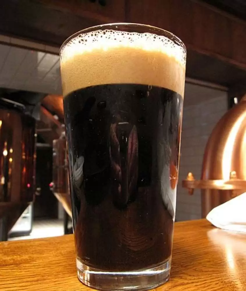 copo de vidro cheio de cerveja preta, em cima de mesa de madeira