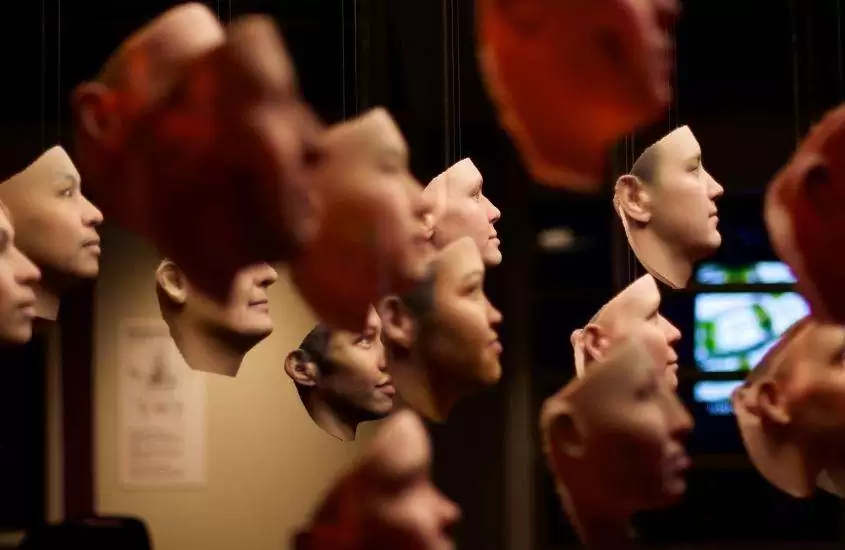 máscaras hiper-realistas de rostos humanos, penduradas em exposição de museu