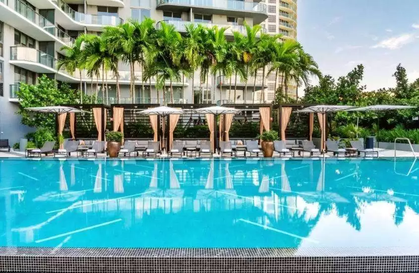 durante o dia, espreguiçadeiras e guarda-sóis brancos em frente a piscina em um dos melhores hoteis em miami