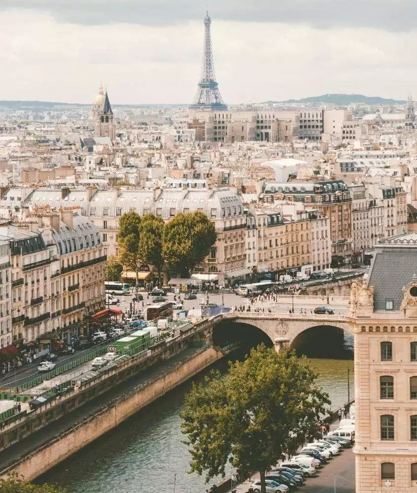 durante o dia, vista aérea de carros estacionados em frente a rio e, ao fundo, construções e Torre Eiffel