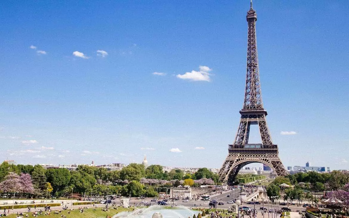 durante o dia, pessoas caminhando em gramado com vista para a Torre Eiffel, torre de treliça de ferro