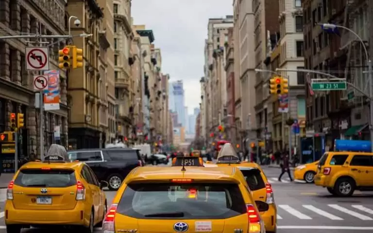 durante o dia, táxis amarelos passando em rua cercada de prédios em rua de nova york eua