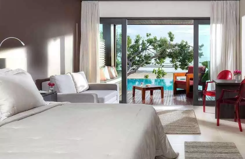 durante dia ensolarado, cama de casal e sofá em suíte de hotel com varanda, piscina privativa e vista para o mar