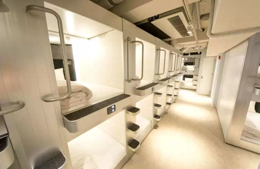 corredor com pequenos quartos brancos de 2 metros de comprimento e 1,25m de largura em um dos hotéis-cápsula em Tokyo Japão