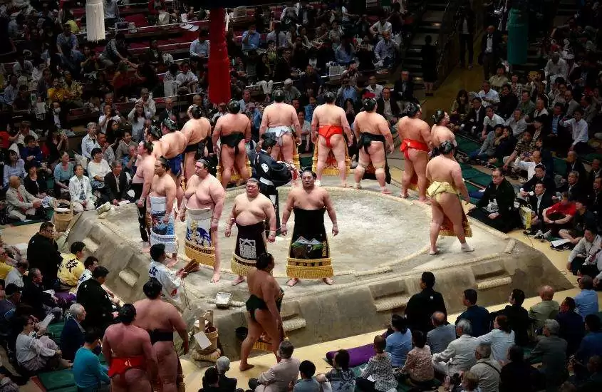 diversos atletas, formando uma roda, em centro de arena de sumô em Tokyo Japão