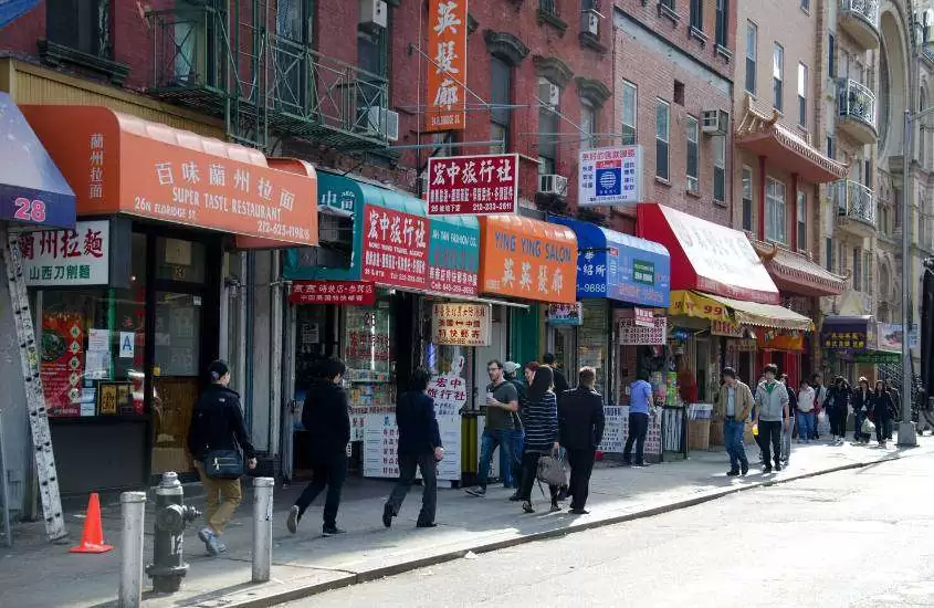 durante o dia, pessoas caminhando em frente a fachada de restaurantes com letreiro em chineses em rua de chinatown