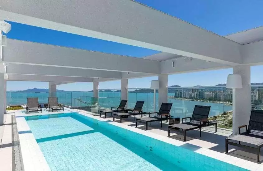 durante o dia, espreguiçadeiras ao redor de piscina ao ar livre em cobertura de hotel com vista para o mar
