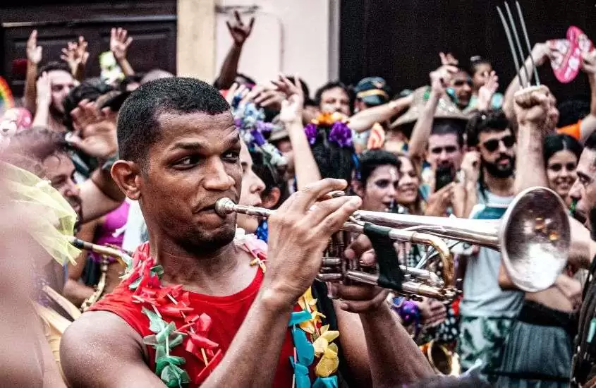 durante o dia, homem com regata vermelha, tocando trompete em bloco de carnaval