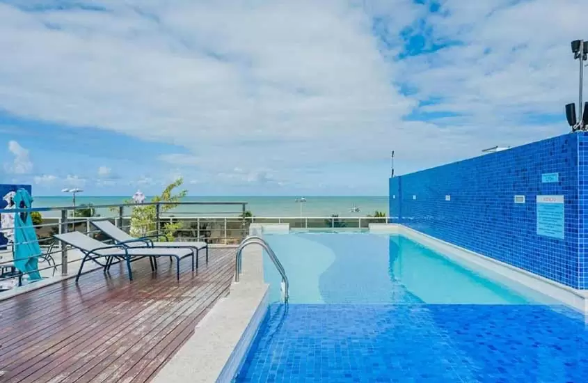 durante o dia, espreguiçadeiras em frente a piscina retangular ao ar livre em cobertura de hotel em João Pessoa com vista para o mar