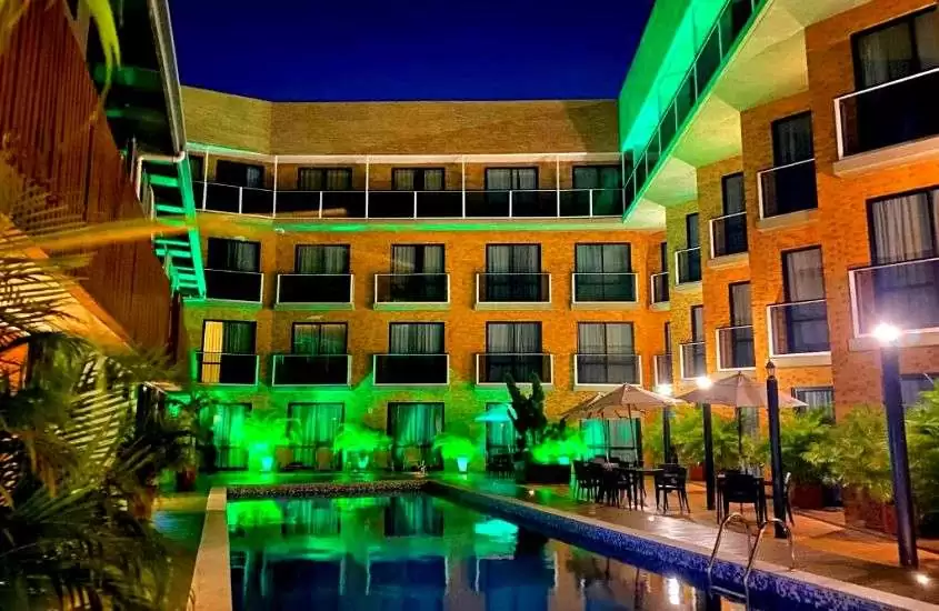 durante a noite, cadeiras e mesas ao redor de piscina, em quintal iluminado por luzes verdes em hotel para passar o ano novo em João Pessoa