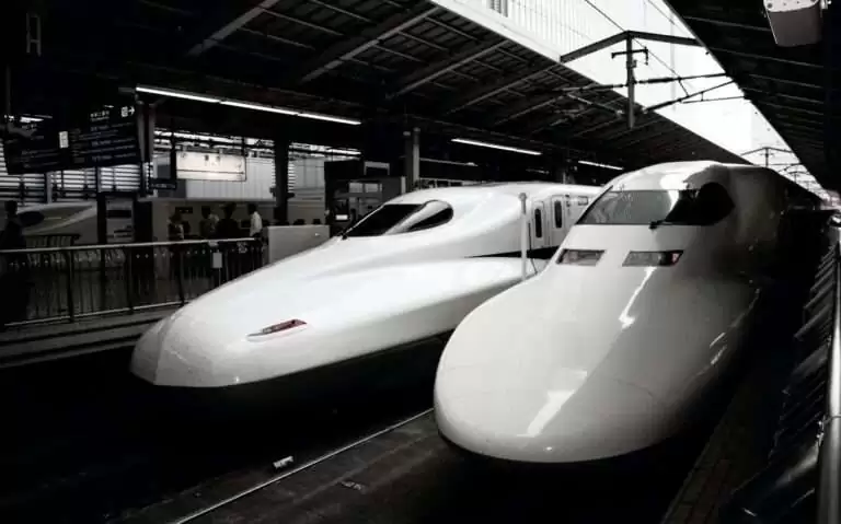 durante o dia, dois shinkansen brancos, parados em estação de trem