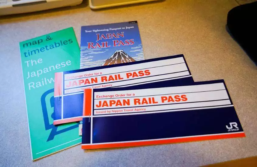 em cima de uma mesa, talão azul, vermelho e branco, onde há escrito 'exchange order for a japan rail pass' e folhetos verdes e azuis