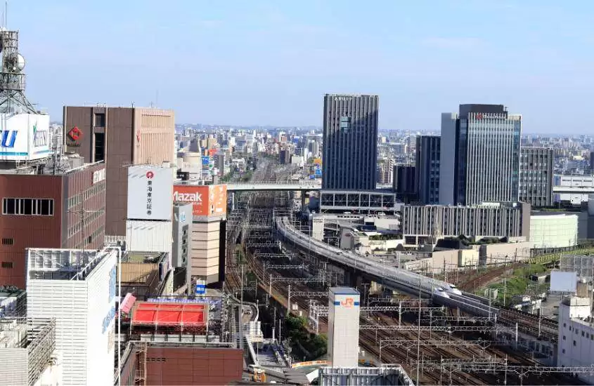 durante o dia, vista aérea de prédios com vista para trilhos onde está passando um trem bala shinkansen