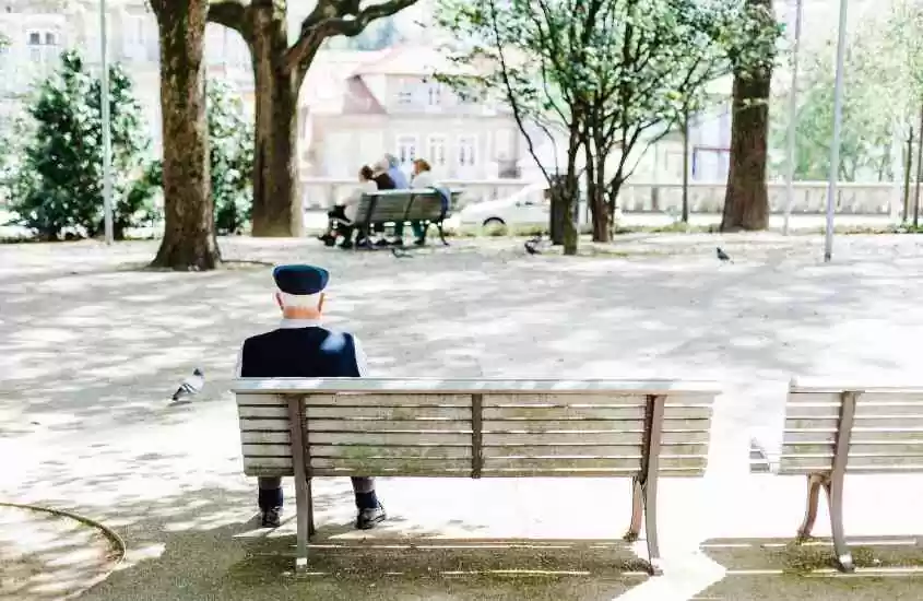 durante o dia, vista de costas de homem idoso sentado em banco de madeira de praça