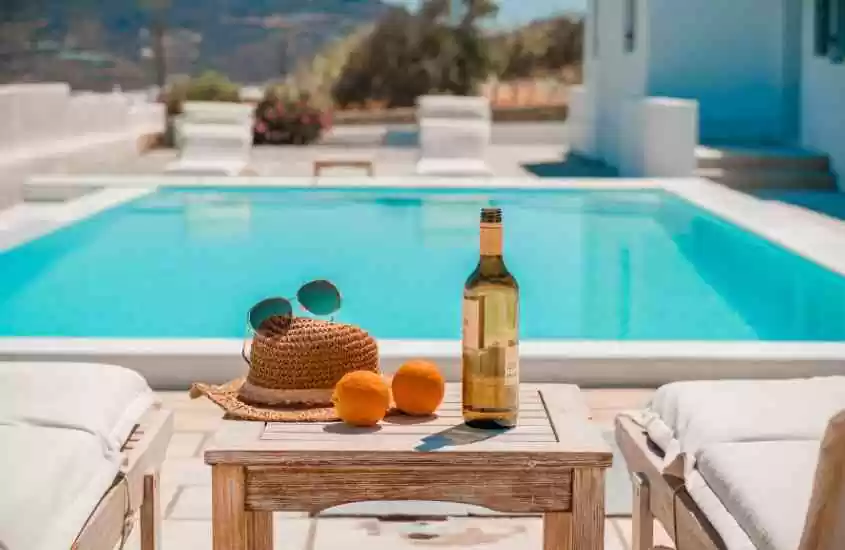 durante o dia, espreguiçadeiras brancas e taça de vinho, chapéu, óculos de sol e laranjas em cima de mesa de madeira, em frente a piscina ao ar livre