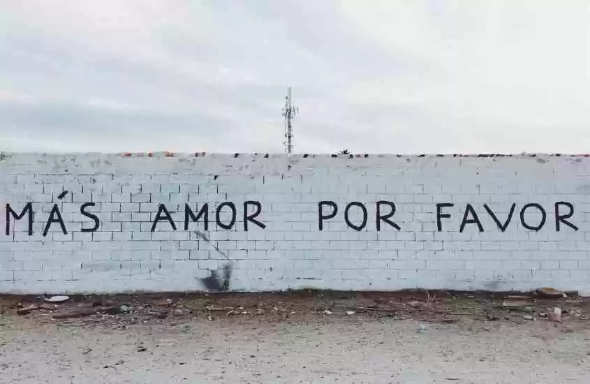 durante o dia, frase ''más amor por favor'' escrita em preto em muro branco