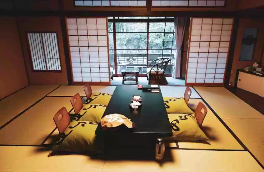 durante o dia, almofadas amarelas ao redor de mesa preta retangular em sala de ryokan no japão com vista para a natureza