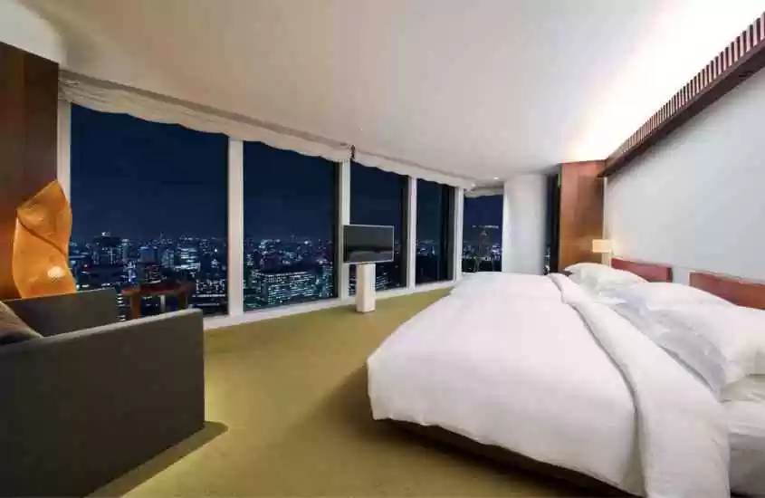 durante a noite, poltrona, cama de casal e tv em suíte de hotel com vista para prédios de tokyo